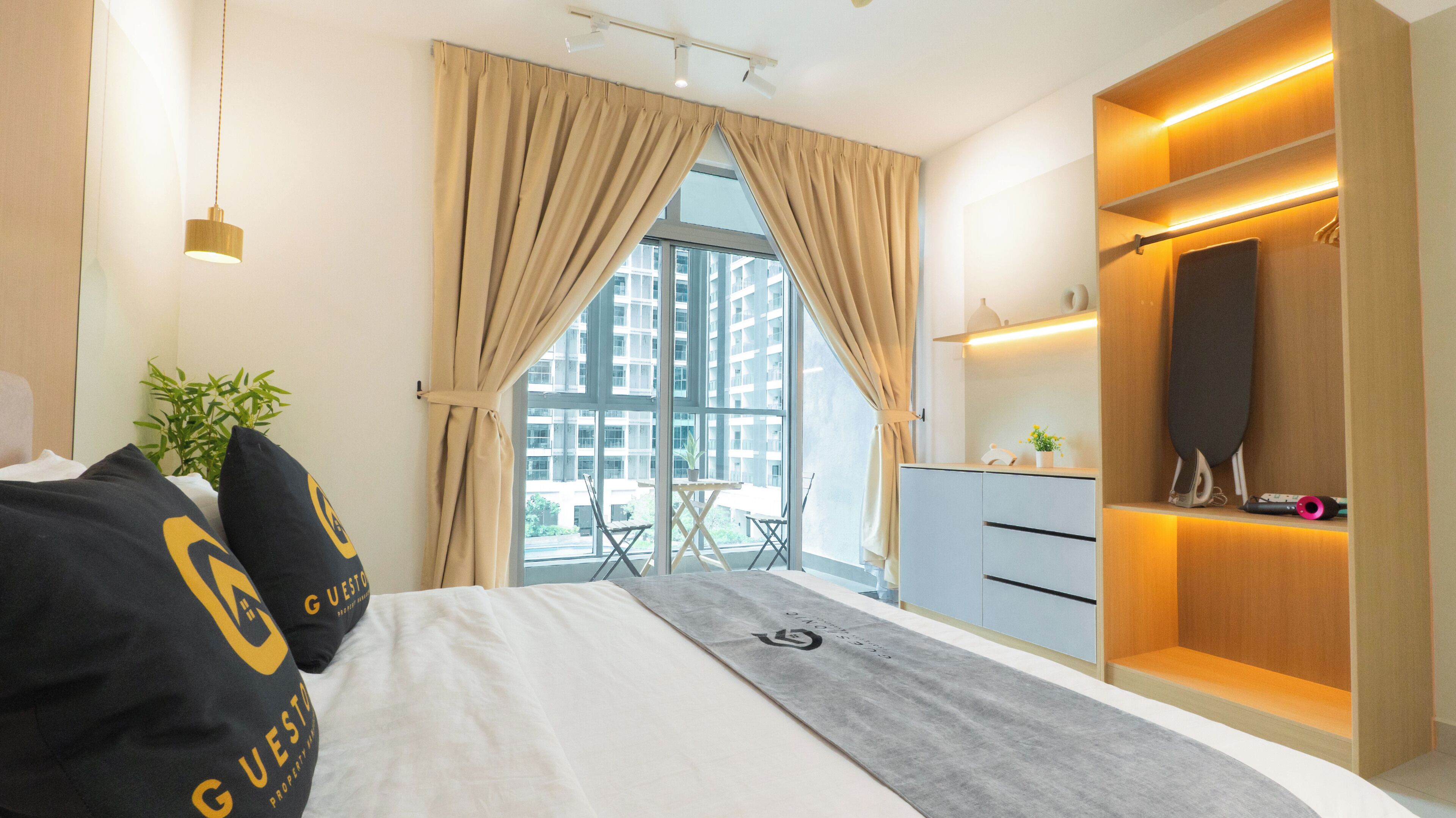 A modern hotel room with a large bed, a desk, a wardrobe, and a view of buildings through the window.