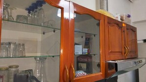 A kitchen with wooden cabinets, glass shelves, and a stainless steel range hood. - Backpackers La Casa De Payaso (Durres)