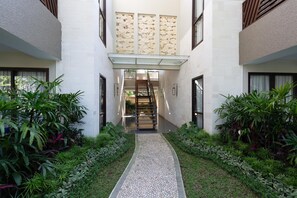 Un bâtiment moderne doté d’un escalier central, entouré d’une végétation luxuriante et bordé d’un chemin pavé de petits galets.