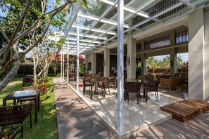 An outdoor patio with glass roofing, wooden furniture, and a garden view. - The Gantari Ubud Bali (Ubud)