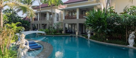 A resort with a swimming pool, a statue, and a two-story building with balconies.