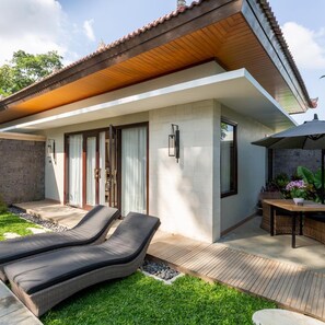 Une maison moderne dotée d’un patio, de deux fauteuils de jardin et d’un coin repas avec une table et un parasol.