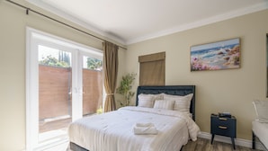 A bedroom with a bed, a nightstand, a painting, and a sliding glass door.