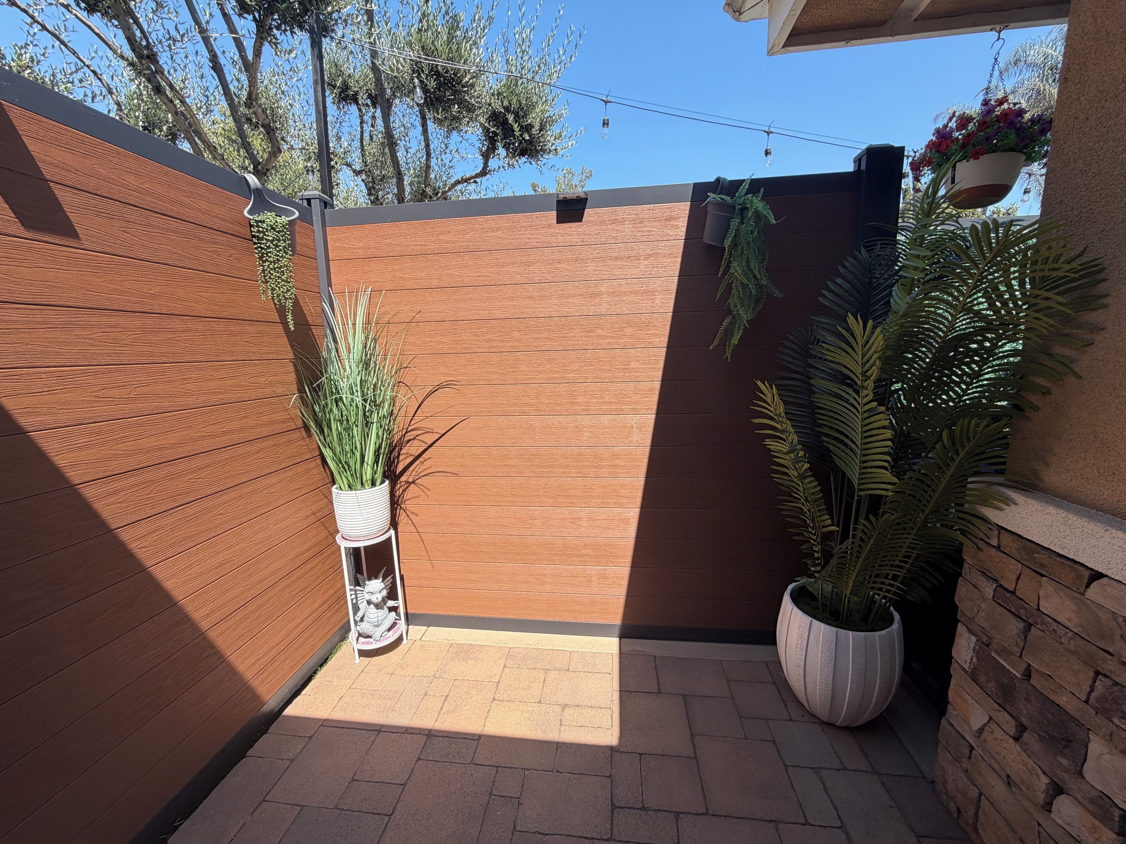 Une clôture en bois, des plantes en pot et une petite statue.