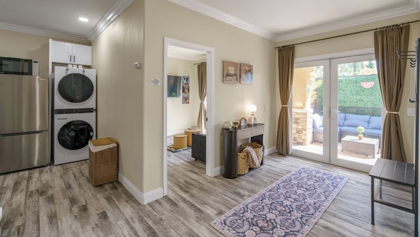 A laundry area with a washing machine and dryer, a small wicker basket, and a hallway leading to a patio with outdoor furniture.