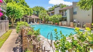 Zona de piscina residencial con una piscina azul cristalina, rodeada de vegetación y un muro de ladrillo.
