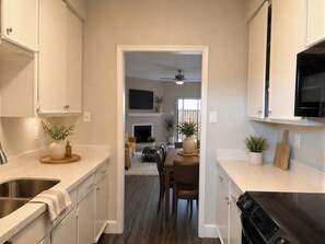 A kitchen with a stove, sink, and cabinets, leading to a dining area with a table and chairs.