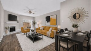 Una sala de estar con sofá, mesa de centro, televisor, chimenea y comedor con mesa dispuesta para cuatro.