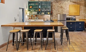 A kitchen with a large island, bar stools, a brick wall, and a stainless steel refrigerator.