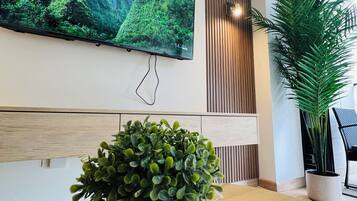 Un interior moderno con un televisor de pantalla plana grande montado en la pared, una mesa de madera y una planta en maceta.