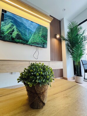 A modern interior with a large flat-screen TV mounted on the wall, a wooden table, and a potted plant. - Apartment in Santiago de Surco with pool and gym (Santiago de Surco)