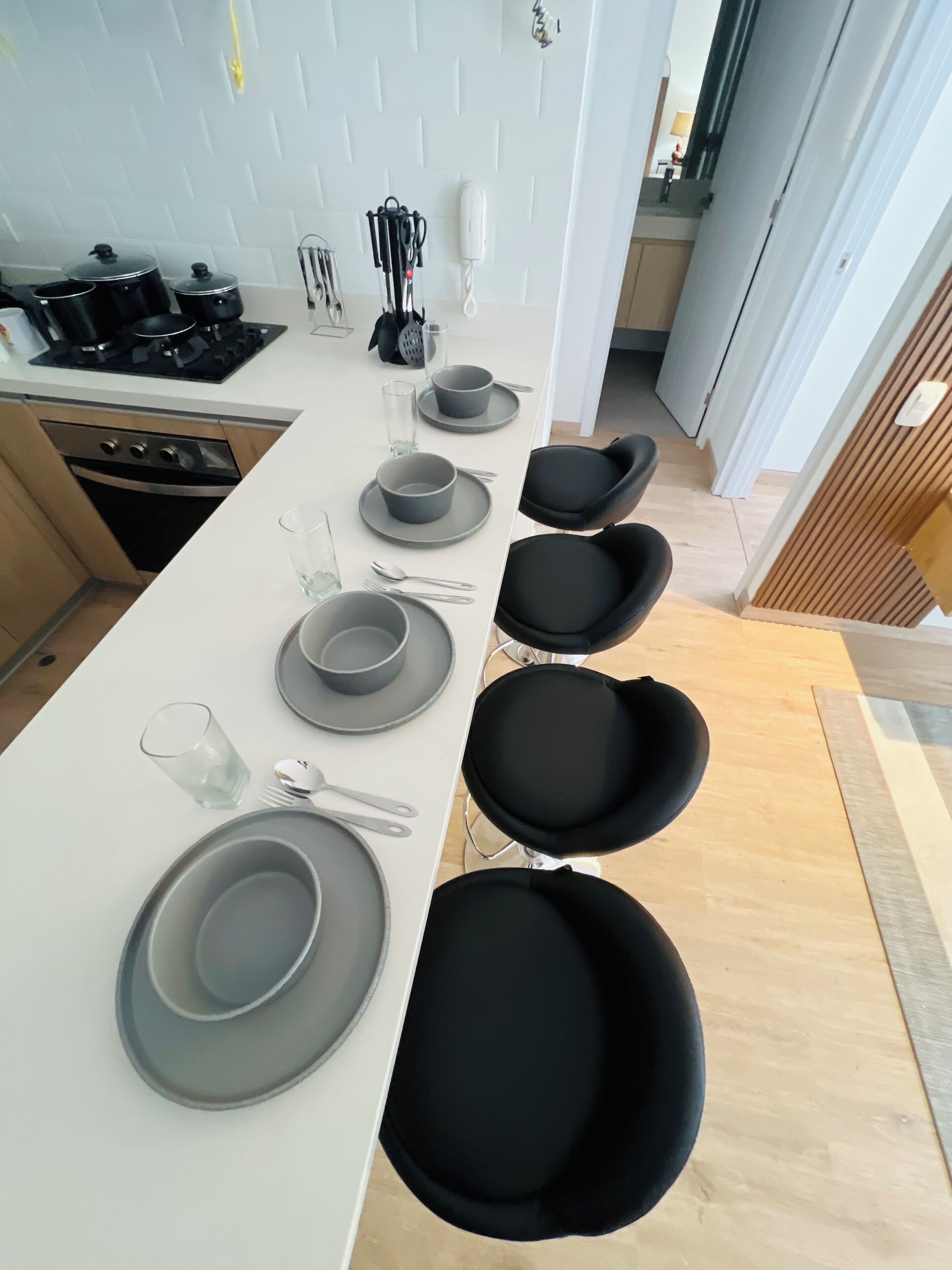 A modern kitchen with a dining area, including a stove, pots, a phone, and a dining table set with plates and chairs.
