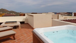 A rooftop terrace with a hot tub, lounge chairs, and a view of the surrounding buildings and hills. - 3-Bedroom Villa - Quivira Los Cabos (Cabo San Lucas)