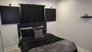 A bedroom with a bed, black curtains, a headboard, and a wall-mounted shelf with a plant. - Cozy 1-bedroom apartment in lovely Dallas with AC (Dallas)