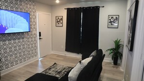 A living room with a sofa, a television, patterned wallpaper, and a potted plant. - Cozy 1-bedroom apartment in lovely Dallas with AC (Dallas)