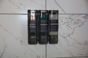 Tres botellas de gel de baño, champú y acondicionador sobre una pared de baldosas.