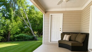 A covered porch with a white door, a dark-colored sofa with cushions, and a concrete floor. -      Walk to Downtown Madison Near Redstone & NASA (Madison)