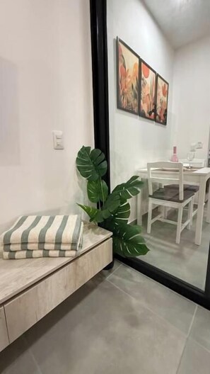 A modern room with a large mirror, a dining table with chairs, a potted plant, and a striped cushion on a bench. - Coralina Paraíso Suite (Santa Marta)