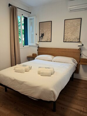 Ein Schlafzimmer mit hölzernem Kopfteil, einem Bett mit weißer Bettwäsche, zwei Nachttischen mit Lampen und zwei gerahmten Bildern an der Wand.