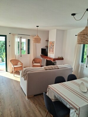 Ein Zimmer mit einer Couch, einem Esstisch, Korbstühlen, einem Fernseher und einem Bild an der Wand.