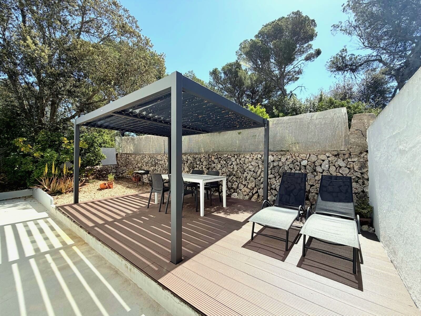 Eine Außenpatio mit einer Pergola, einer Steinmauer und einer Sitzgelegenheit.