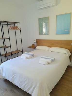 A neatly made bed with white linens, a wooden headboard, and two towels. There is a black metal shelf unit with wooden hangers to the left. - Can Andreu II apartment next to the beach (Cala Galdana)