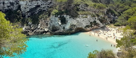 Una zona costera con playa, acantilados rocosos y agua turquesa cristalina.