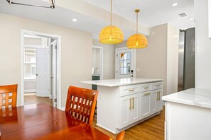 A modern kitchen with white cabinetry, a wooden dining table, and two pendant lights. - Modern 5BR | 1.5 Blks 2 Beach | Beach Gear&Games (Atlantic City)