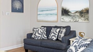 Ein Wohnzimmer mit grauem Sofa, gemusterten Kissen und drei gerahmten Bildern an der Wand.