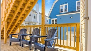 Eine Holzterrasse mit Adirondack-Stühlen, einem Hollergeländer und Blick auf ein blaues Gebäude.