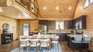 Una cocina amplia con paredes de madera, una zona de comedor con alfombra a cuadros y una escalera que sube a un nivel superior.