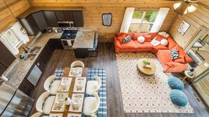 Una cabaña de madera pequeña y acogedora con cocina, comedor y sala de estar, que cuenta con un ventanal grande y un ventilador de techo.