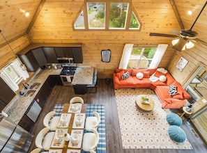 Eine gemütliche Holzhütte mit Küche, Essbereich und Wohnbereich, ausgestattet mit einem großen Fenster und einem Deckenventilator.