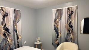 A room with a bed, a chair, a small table with a decorative item, and curtains with abstract designs. - Tranquil 3-bedroom house in Syracuse perfect for your getaway (Syracuse)