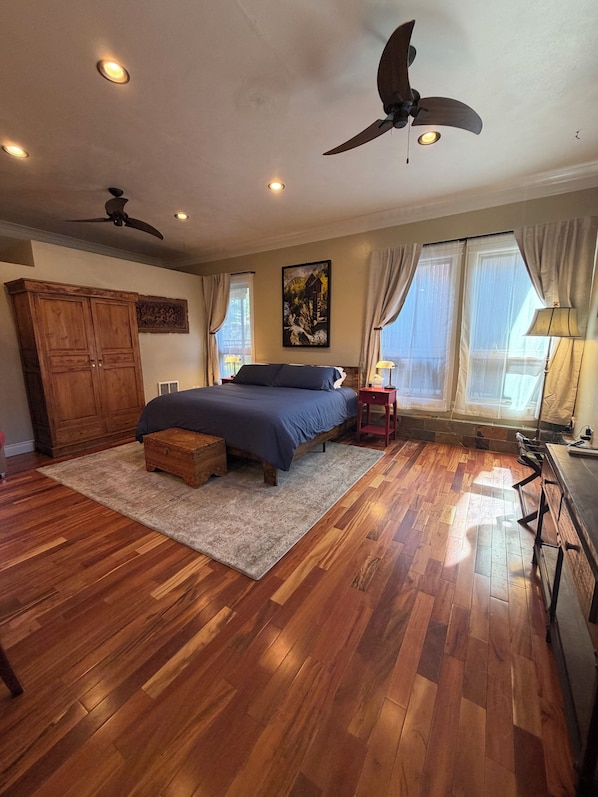 Un dormitorio con una cama, armario de madera, ventiladores de techo y un cuadro en la pared.