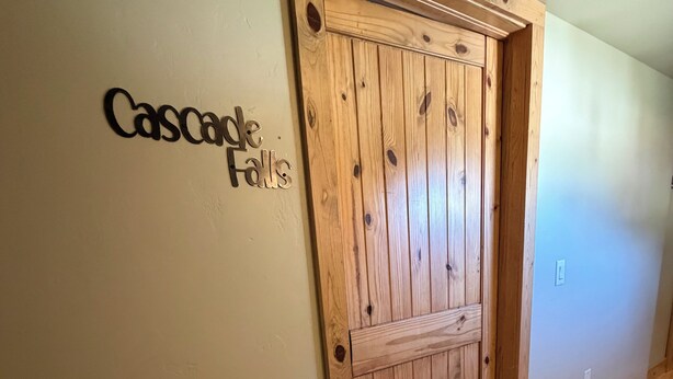 En dörr av trä med en välkomstmatta framför och en skylt med texten ”Cascade Falls” på väggen.