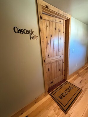 Een houten deur met een 'Welcome' welkomstmat en een bord met daarop 'Cascade Falls'.