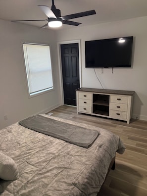 Ein Schlafzimmer mit Bett, Deckenventilator, Fernseher, Tür und Kommode.