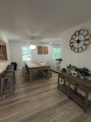 A modern living space with a dining area, a sofa, a wooden coffee table, and a wall clock.