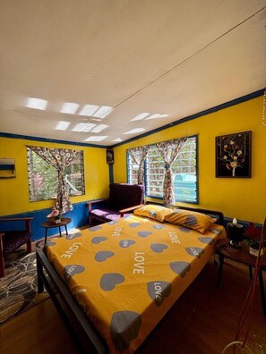 Ein Zimmer mit einem Bett, einem Sessel, einem kleinen Tisch und einem Fenster mit Vorhängen.