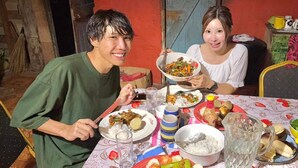 Two people seated at a table with various dishes, a bottle, and a pitcher.