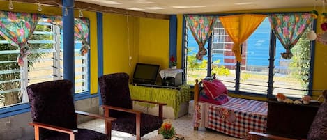 A room with a ceiling fan, two chairs, a small table with a tablecloth, and a window with curtains.
