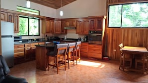 A kitchen with wooden cabinets, a refrigerator, a microwave, a stove, and a bar area with stools. - Spacious Monteverde Bird-watchers Home (Monteverde)