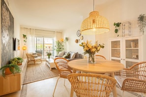 A modern living room with a round wooden table, wicker chairs, a large hanging light fixture, and a white cabinet with glass doors. - Calanova Grand Golf, La Cala de Mijas, Spain (La Cala de Mijas)