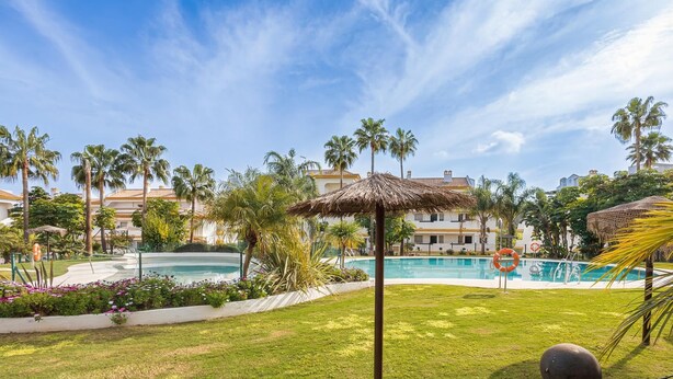 Zona de piscina amb palmeres, una sobrada de palla i un flotador.