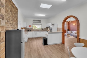 A modern kitchen with white cabinets, a black refrigerator, and a wooden floor. - Charming Family Retreat with Arcade + Walk to Shops - Glenunga (Glenunga)