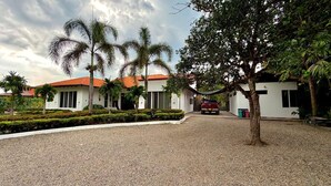 A building with a gravel driveway, palm trees, and a red-roofed structure. - Luxury house in Villavicencio, just 10 mins from the city surrounded by nature. (Villavicencio)