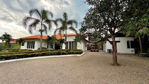 Un edificio con camino de grava, palmeras y una estructura de techo rojo.