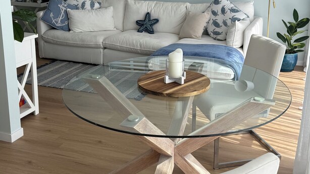 A modern living room with a glass coffee table, a white sofa with patterned cushions, and a floor lamp.