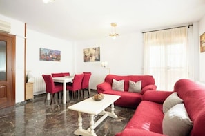A living room with a red sofa, a dining table with red chairs, a white coffee table, and a chandelier.